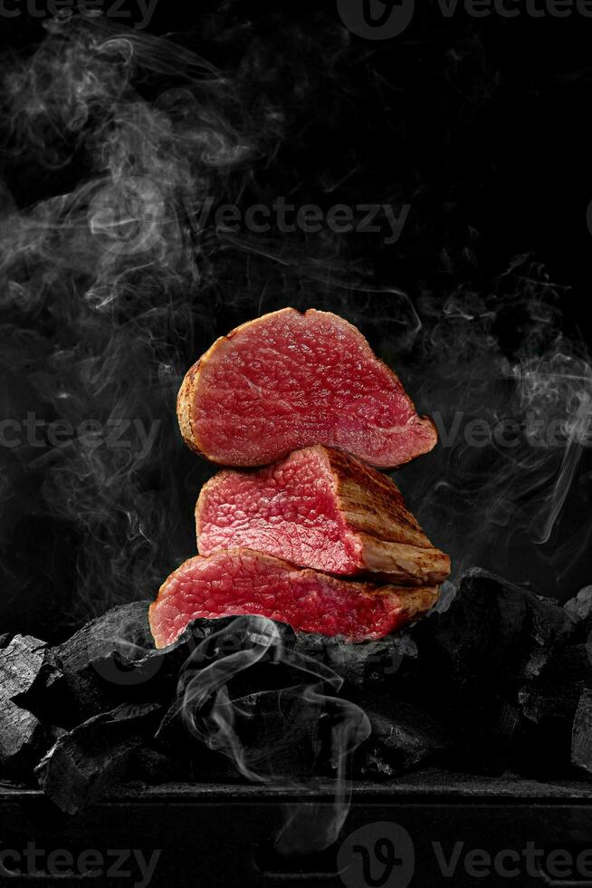 tranché rare veau filet sur charbons sur noir Contexte dans blanc fumée photo