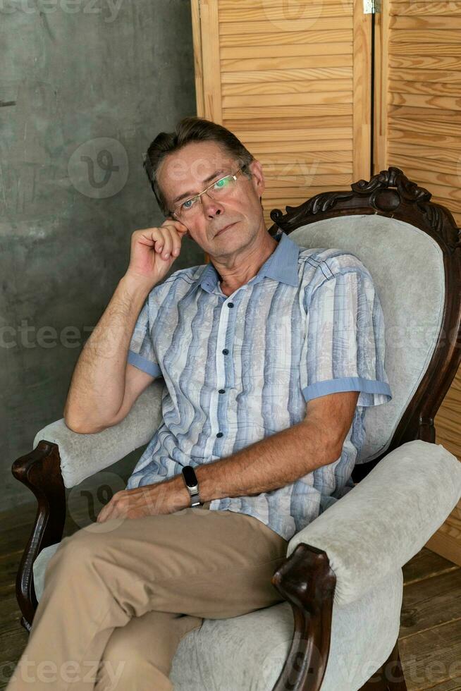 un vieux intelligent homme ayant une du repos sur une fauteuil photo