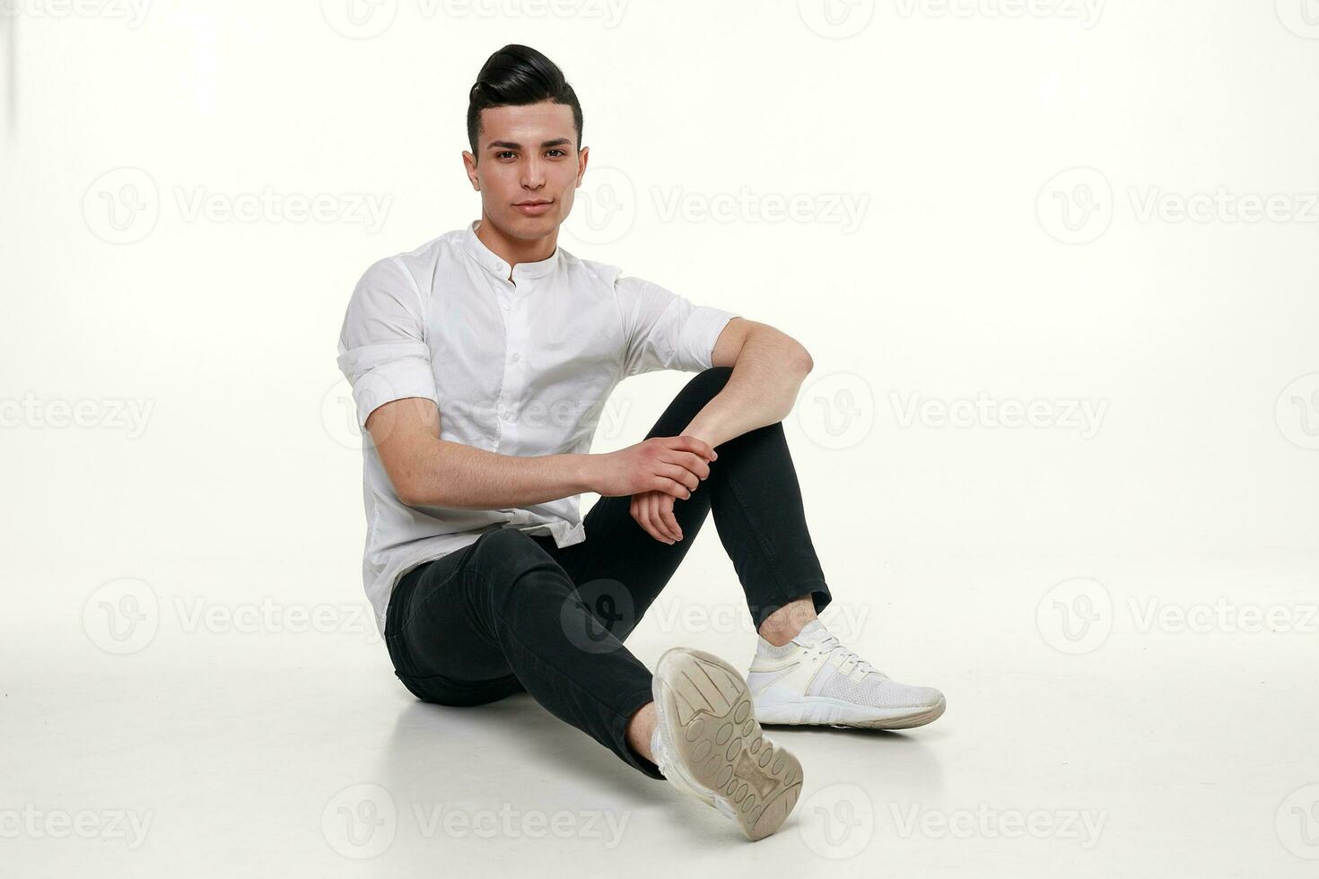 beau, jeune, branché homme est séance sur le sol dans studio photo