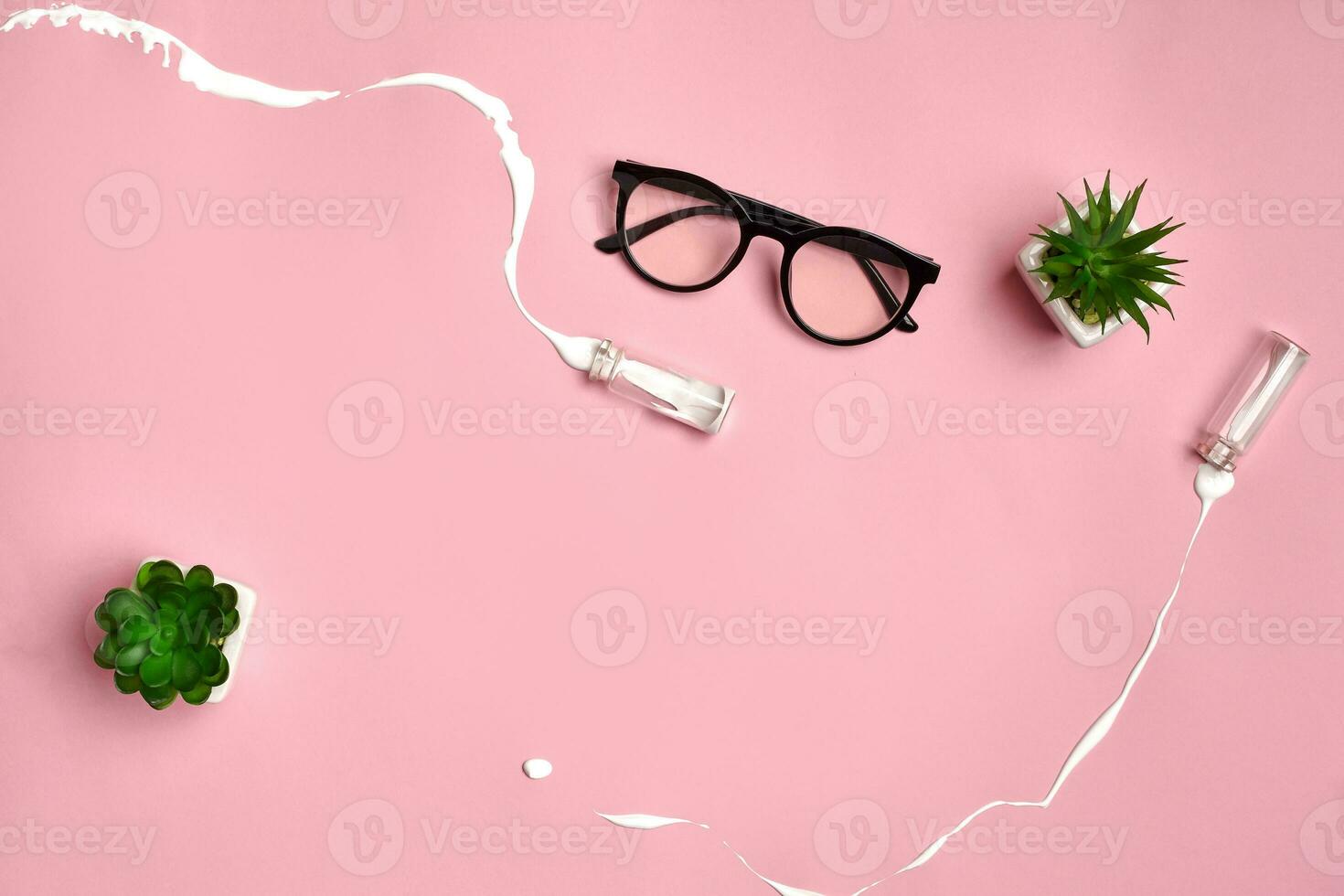 lunettes, vert plantes succulentes et deux petit verre bouteilles de lequel déversé blanc liquide sur rose studio Contexte. proche en haut, copie espace photo