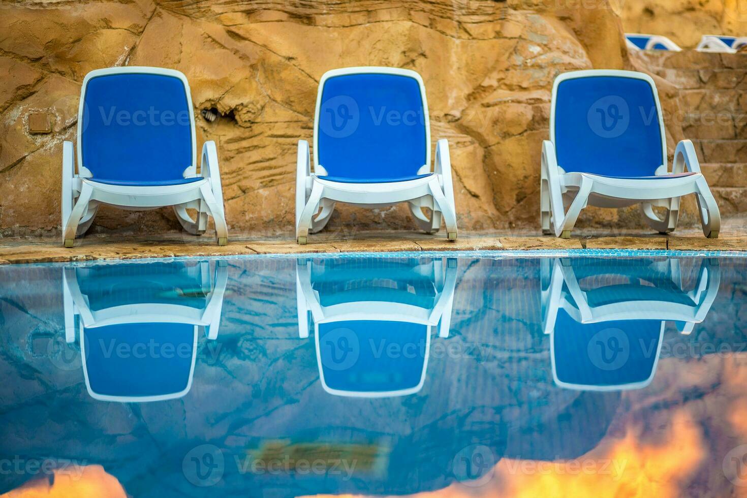 chaises longues près nager bassin et réfléchi leur dans bleu l'eau photo