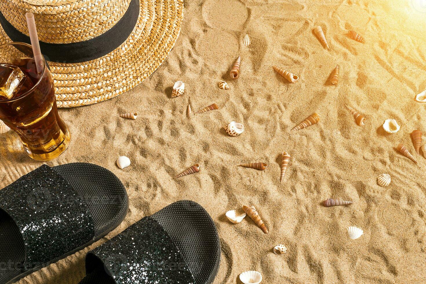 été tenue de plage, retourner flops, chapeau, du froid boisson dans une verre et coquillages sur le sable plage. photo