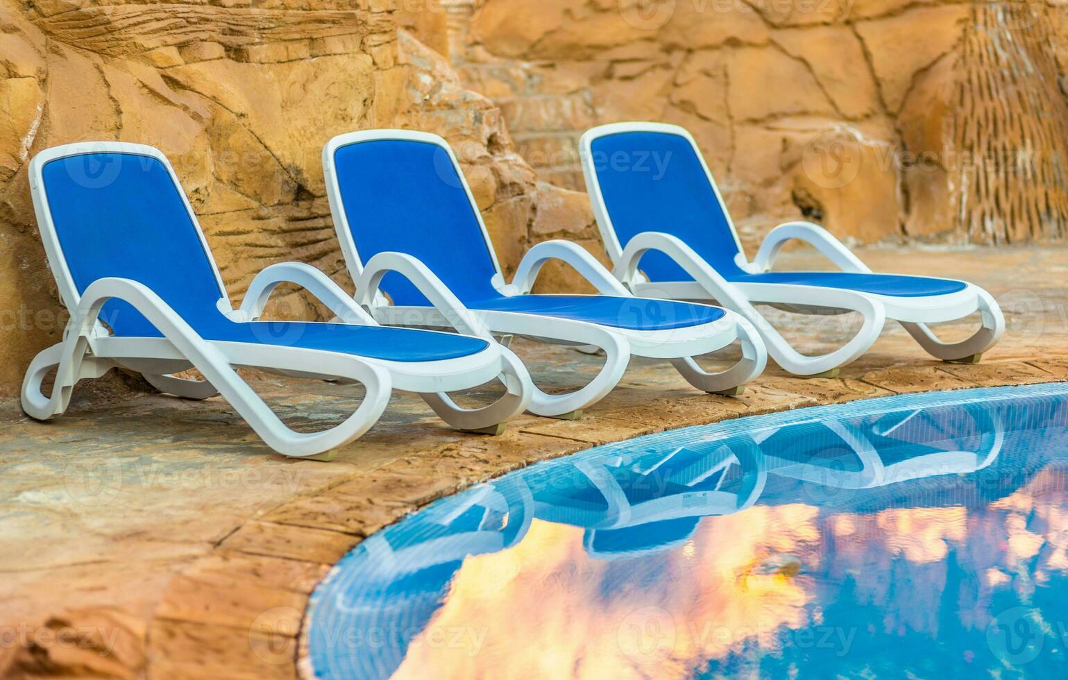 chaises longues près nager bassin et réfléchi leur dans bleu l'eau photo