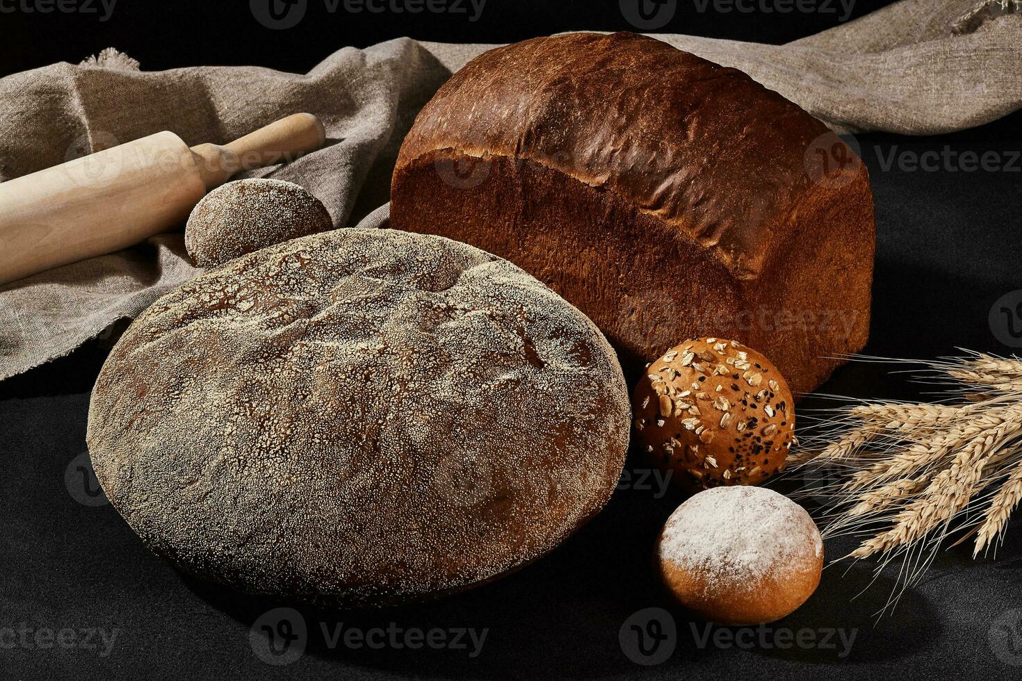 variété de cuit pain et petits pains avec sésame et tournesol graines, saupoudré avec farine. bouquet de blé, toile de jute, roulant broche, noir Contexte. fermer photo