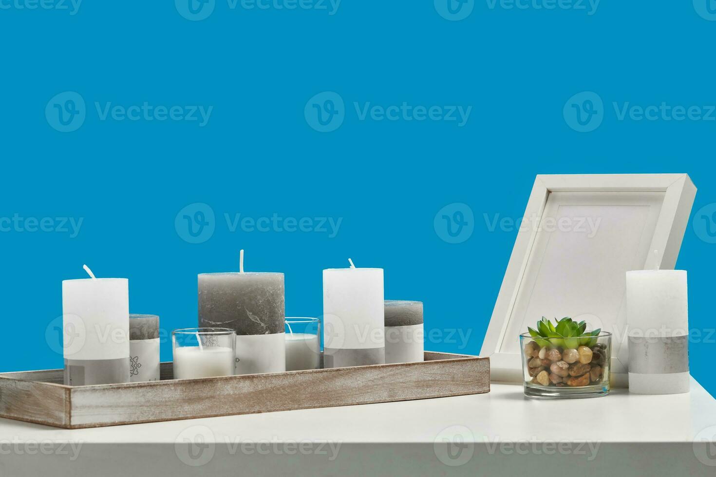 blanc table avec vert succulent dans verre pot, certains différent taille bougies dans une en bois supporter et vide photo Cadre. bleu Contexte. proche en haut