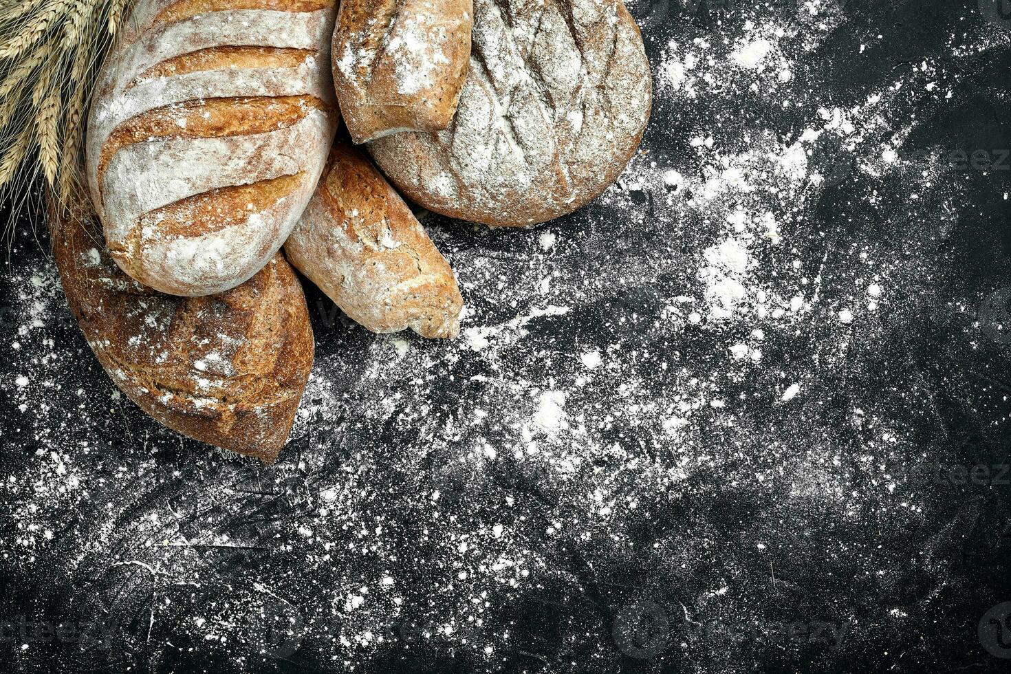 fait maison seigle pain saupoudré avec farine et divers céréales et des graines sur une noir Contexte avec épillets de blé ou seigle et avoine. photo