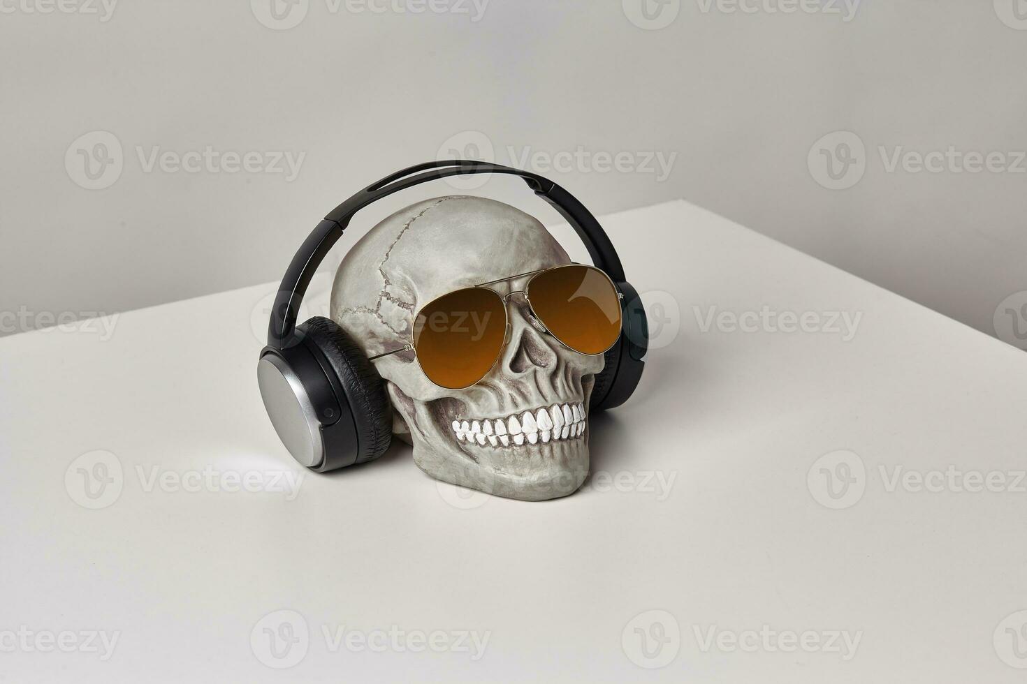 réaliste modèle de une Humain crâne avec les dents dans une des lunettes de soleil et écouteurs sur une lumière tableau, blanc Contexte. médical science ou Halloween horreur concept. photo