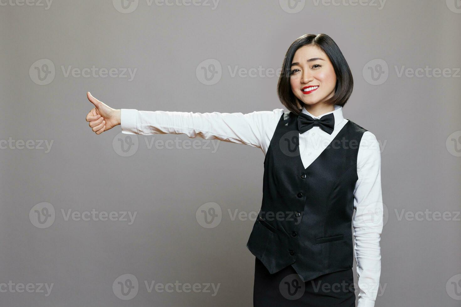 souriant asiatique serveuse montrant pouce en haut geste et à la recherche à caméra avec positif émotion. de bonne humeur femme réceptionniste exprimer un service approbation et la satisfaction portrait photo