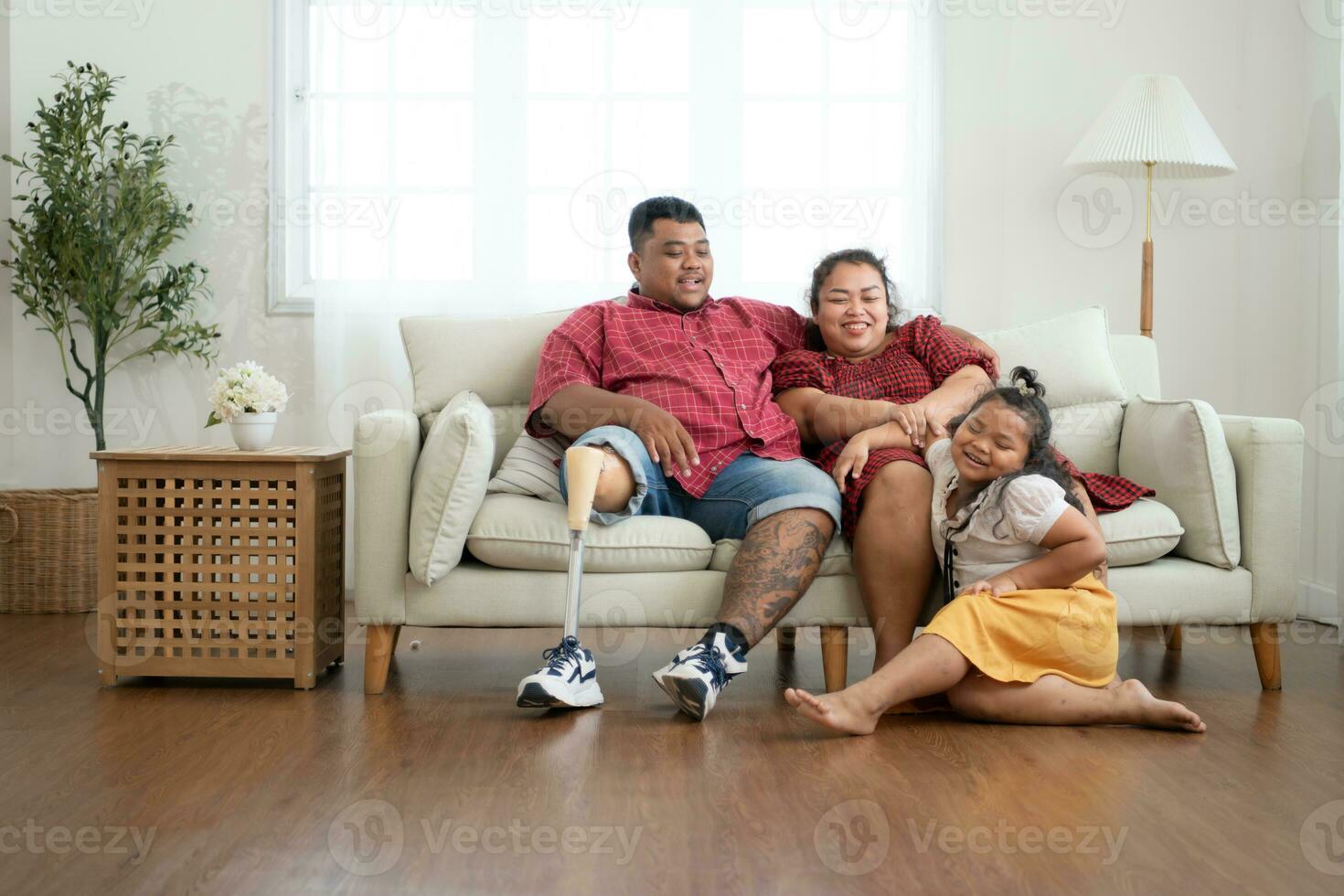 une plus Taille famille avec une père portant une prothétique jambe, repos et parlant avec fille sur le hebdomadaire vacances, dans le vivant pièce de le maison. photo