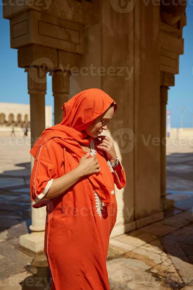 dynamique portrait de une élégant femme dans islamique ethnique tenue, à la recherche bas, permanent entre marbre Colonnes de une mosquée photo