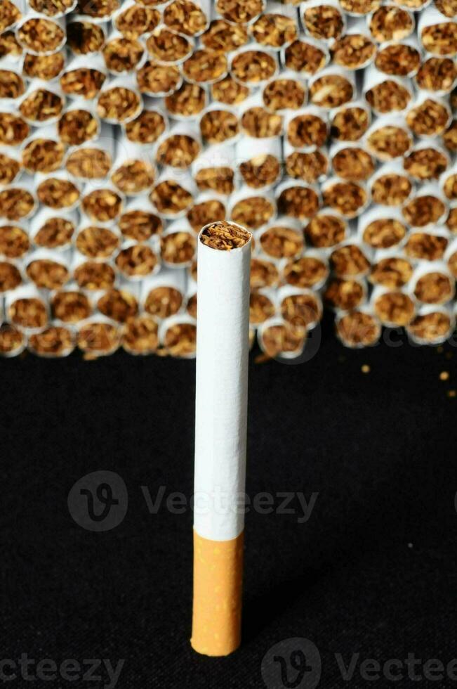 une cigarette est montré dans de face de une pile de cigarettes photo