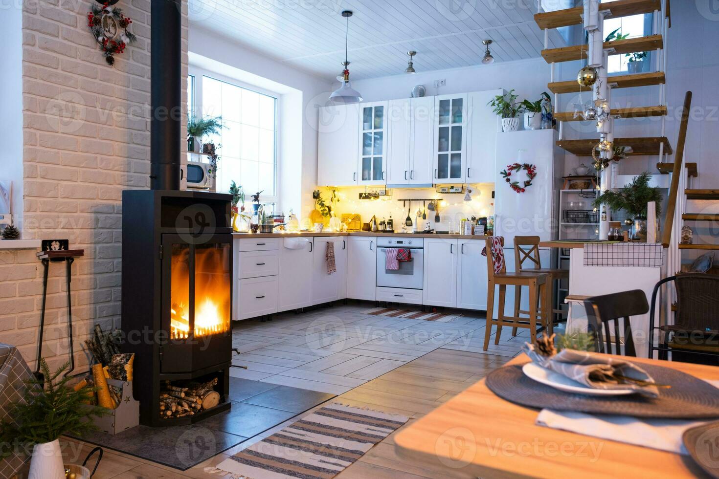 l'intérieur festif de la maison est décoré pour noël et le nouvel an dans un style loft avec poêle noir, cheminée, arbre de noël. chambre studio chaleureuse avec table dressée, feu de bois, cosy et chauffage d'accueil photo