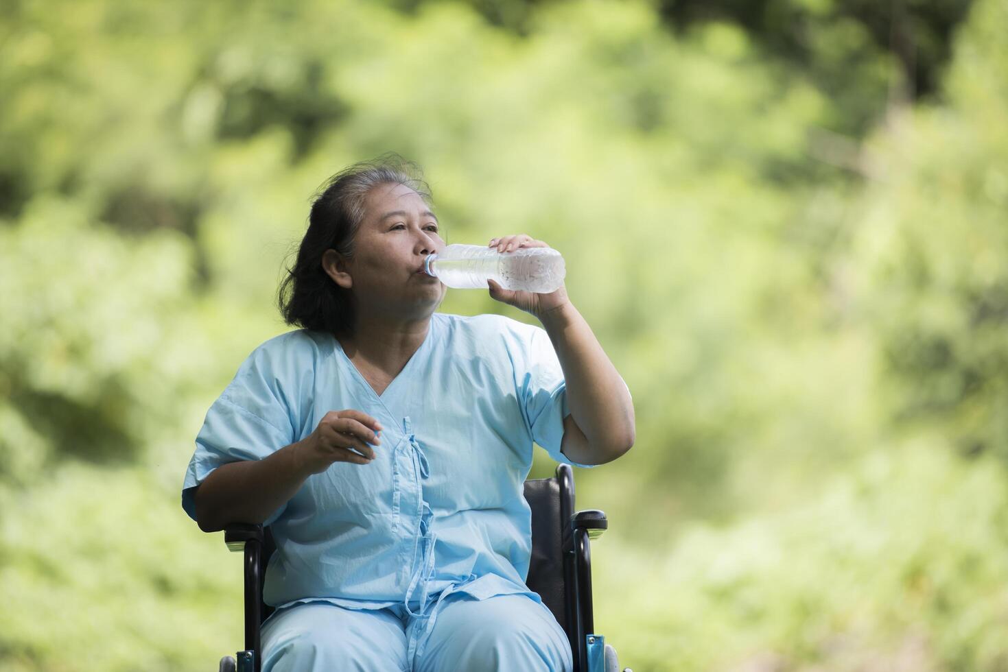 vieille femme s'asseoir sur un fauteuil roulant avec une bouteille d'eau après avoir pris un médicament photo