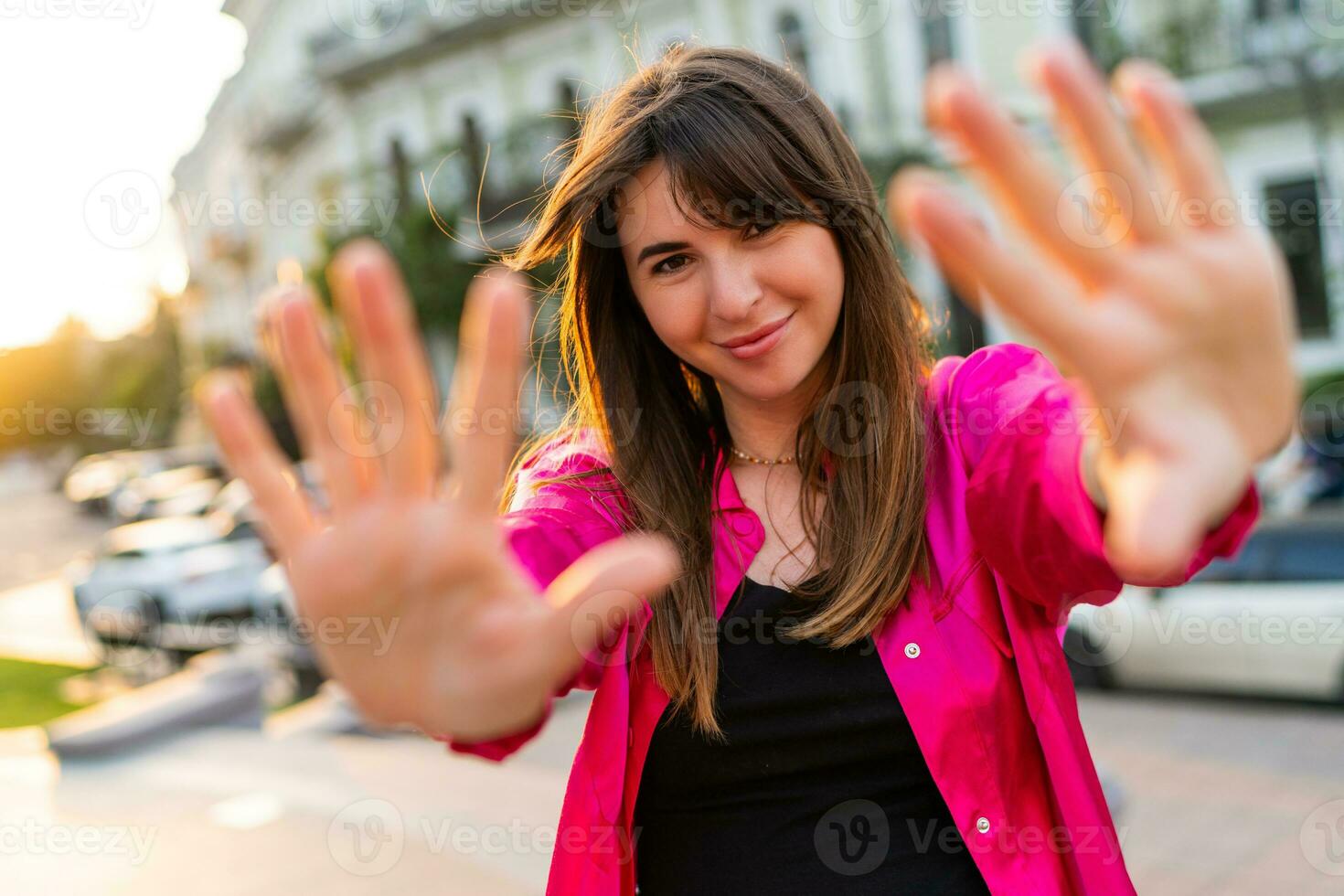 Extérieur été portrait de débonnaire bien regarder femme dans élégant rose merdique. européen rue sur Contexte. chaud le coucher du soleil couleurs. photo