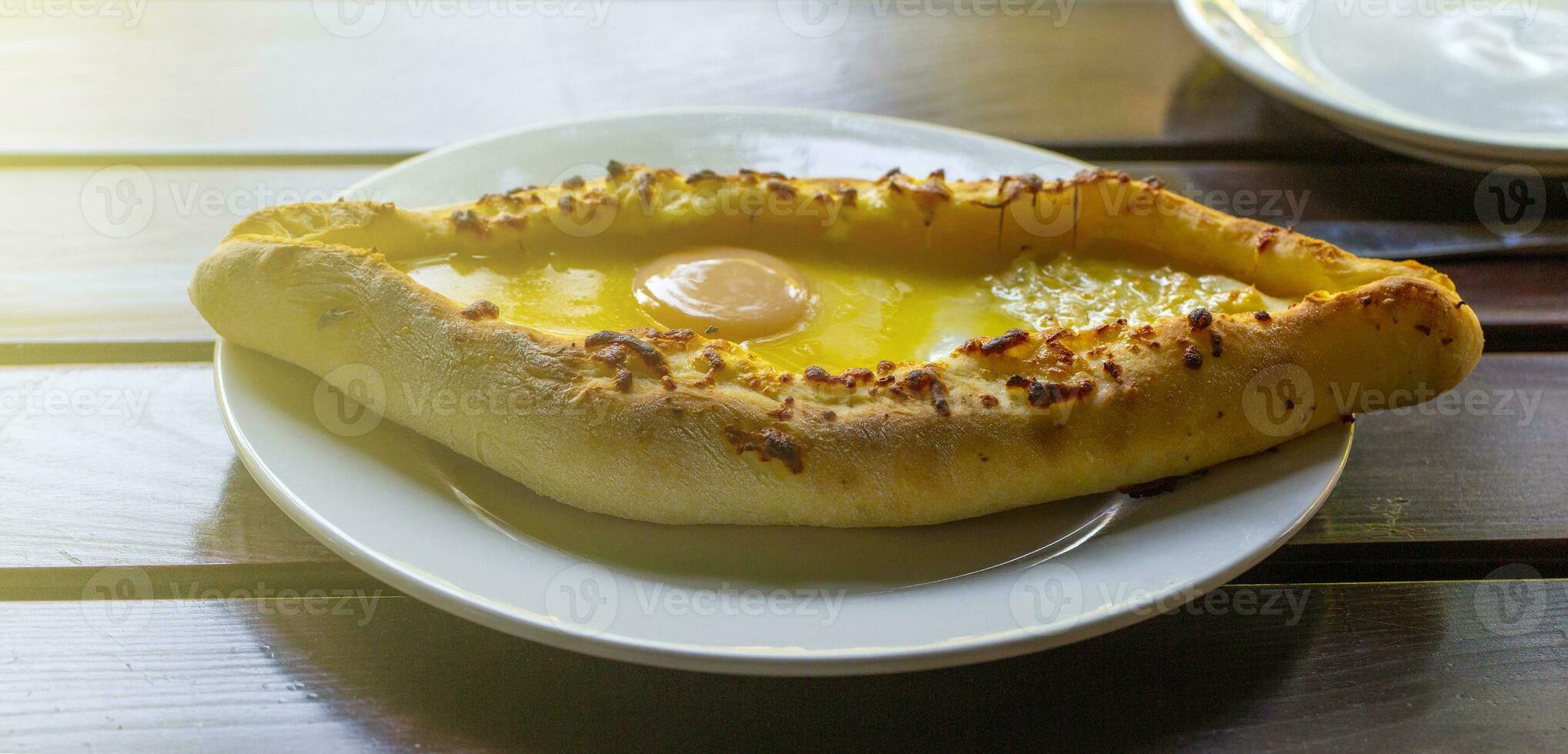 style adjarie khachapuri, cuit pâte avec œuf, fromage et deux pièces de beurre sur une blanc assiette dans une café. photo