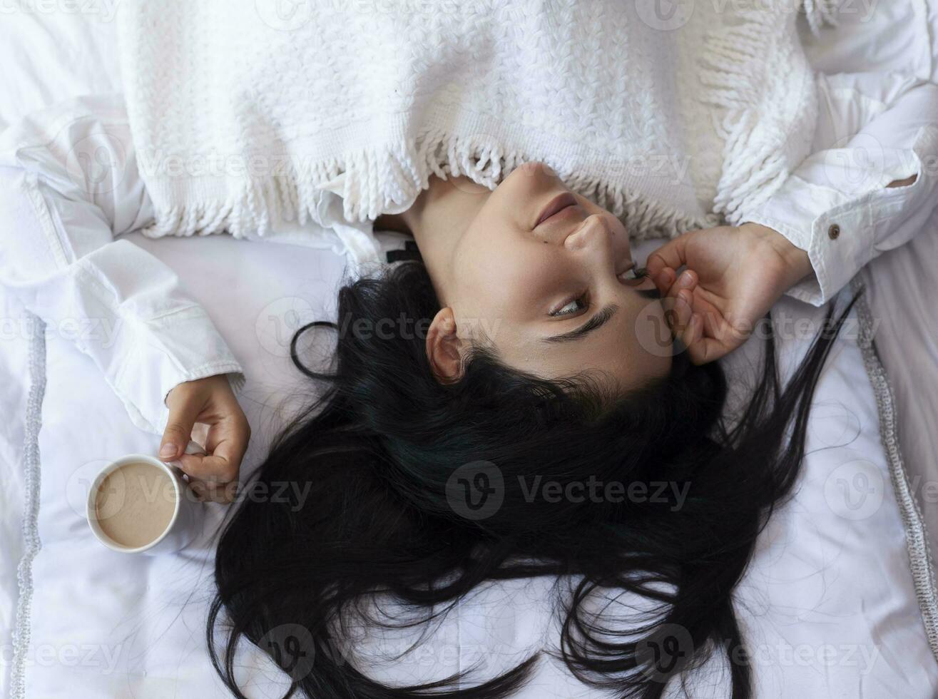 beauté femme en buvant café dans lit après veille en haut dans Matin. Jeune magnifique femme dans lit avec tasse de café. mignonne Dame veille en haut. petit déjeuner dans une confortable chambre photo