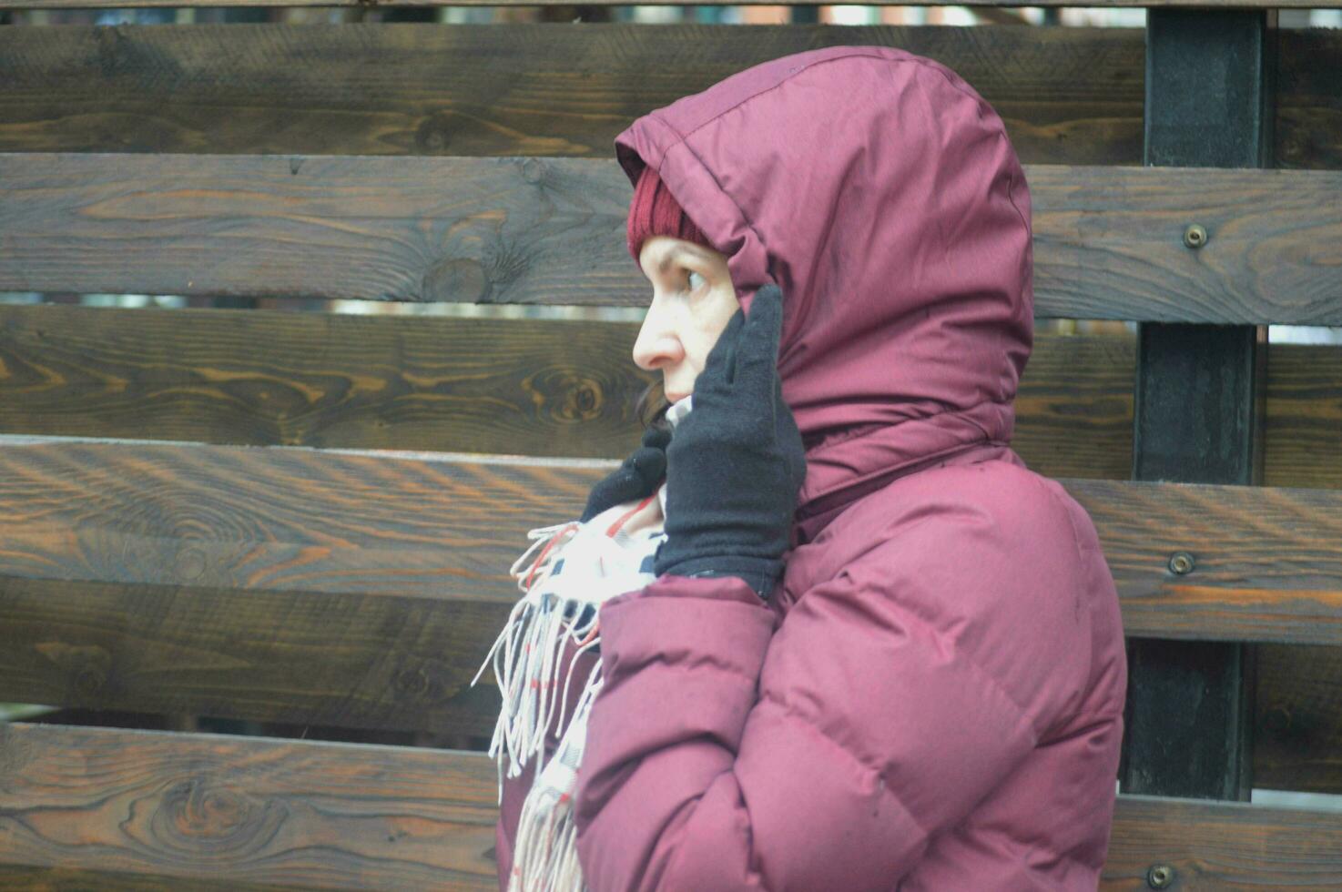 une caucasien femme dans une Bourgogne veste et une à carreaux Jaune écharpe couvertures sa tête et visage avec une capuche de le temps et vent. temps protection. photo