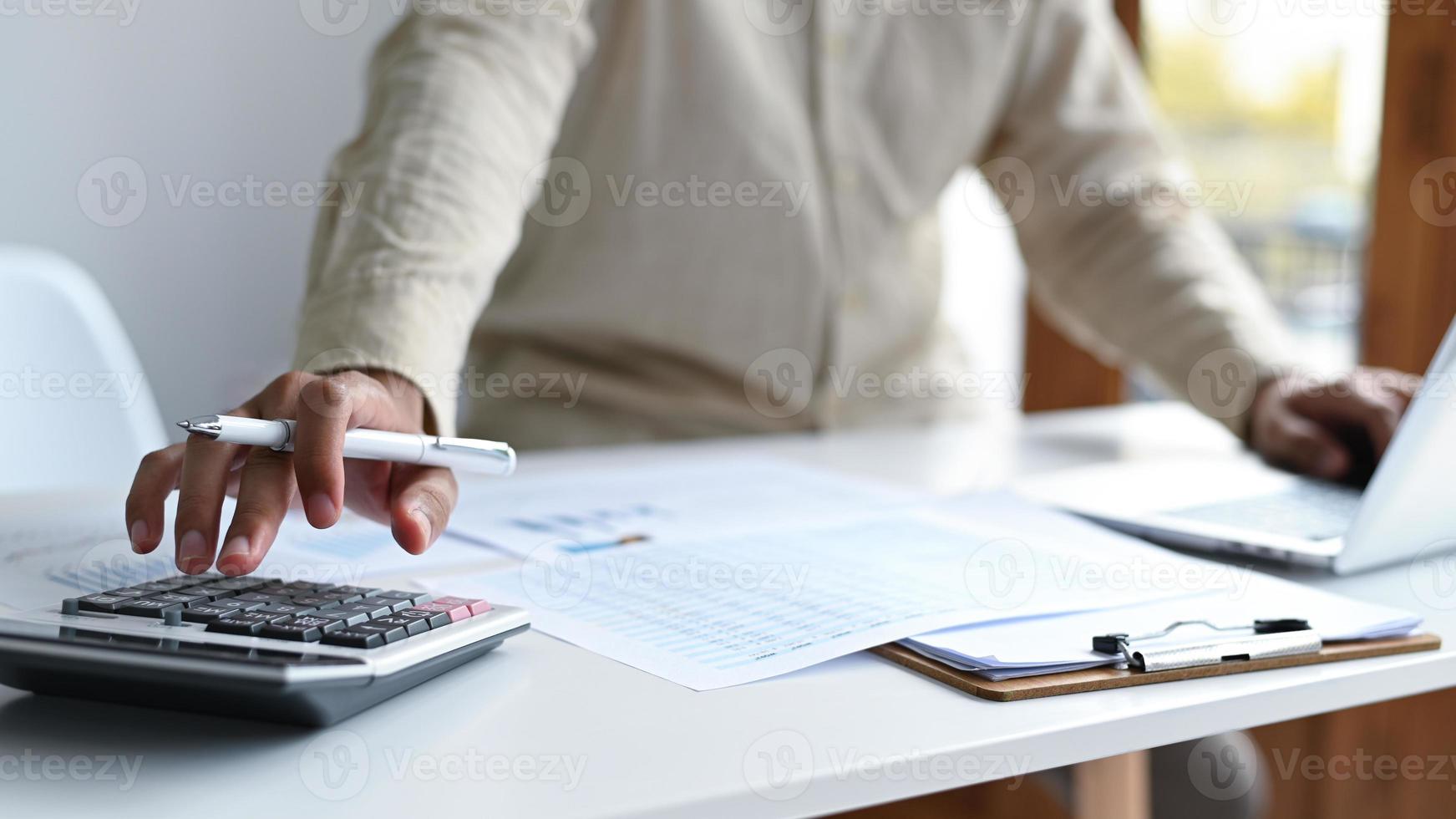 main avec un stylo pour utiliser la calculatrice et le clavier d'ordinateur portable. photo