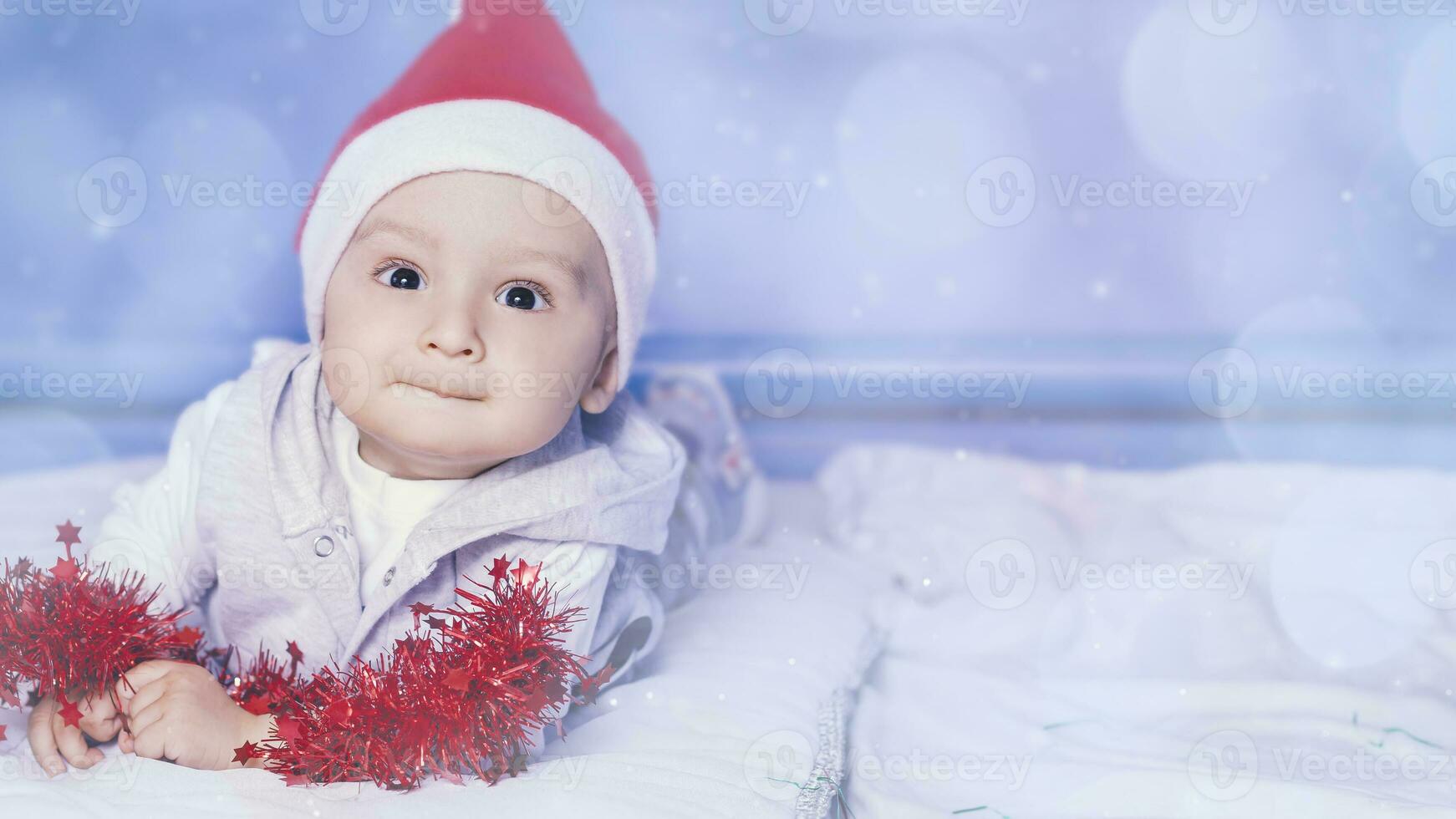 peu marrant Père Noël garçon en jouant avec Noël ou Nouveau année vacances de fête guirlande. 1 année vieux bébé garçon dans Père Noël claus casquette. photo