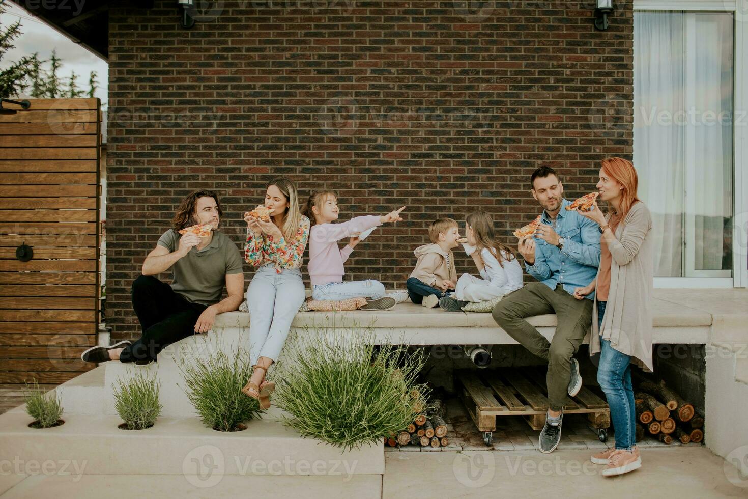 groupe de Jeune gens et des gamins en mangeant Pizza dans le maison arrière-cour photo