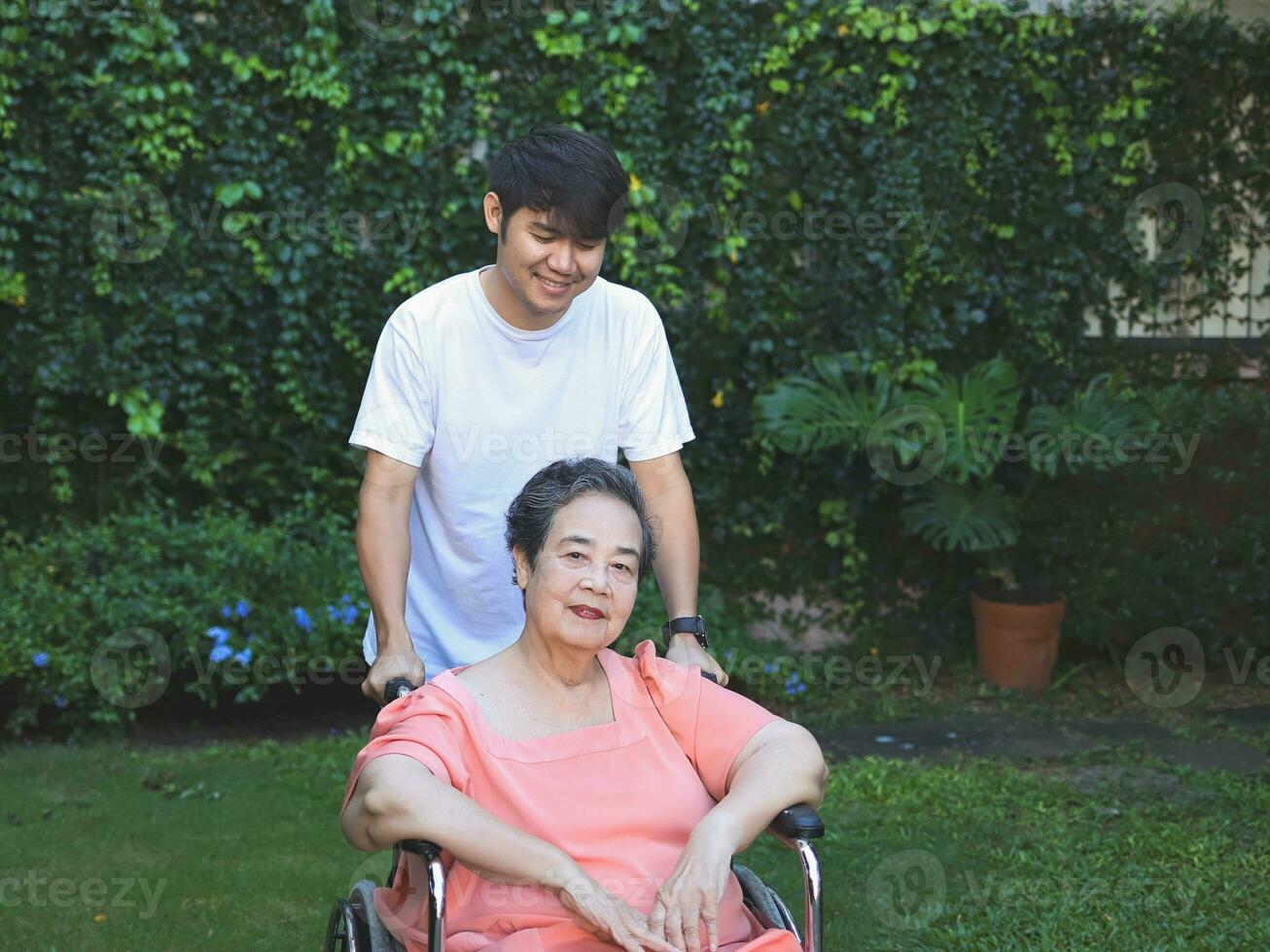 asiatique Sénior femme séance sur fauteuil roulant avec sa fils dans le jardin. photo