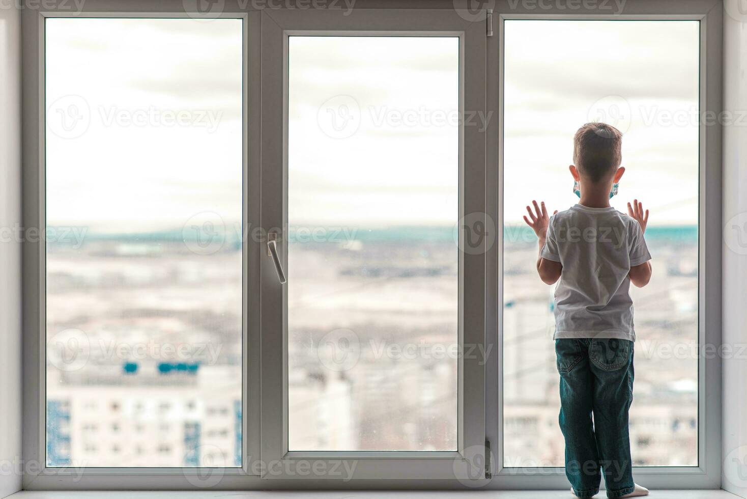 une enfant dans une médical masque est séance à Accueil dans quarantaine car de coronavirus et convoitise -19 et regards en dehors le la fenêtre. photo