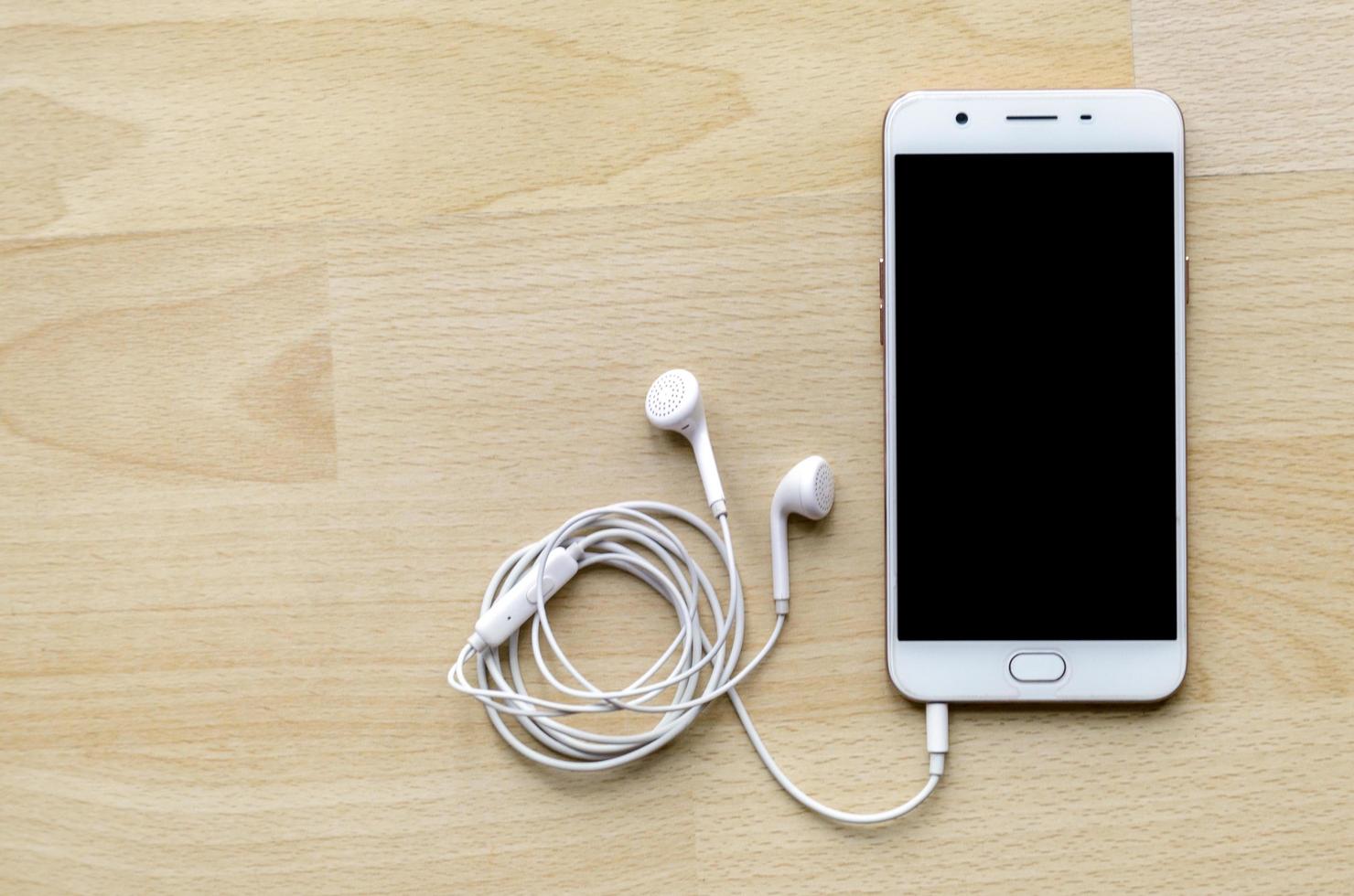 Smartphone à écran blanc avec écouteur sur le coin supérieur de la table en bois photo