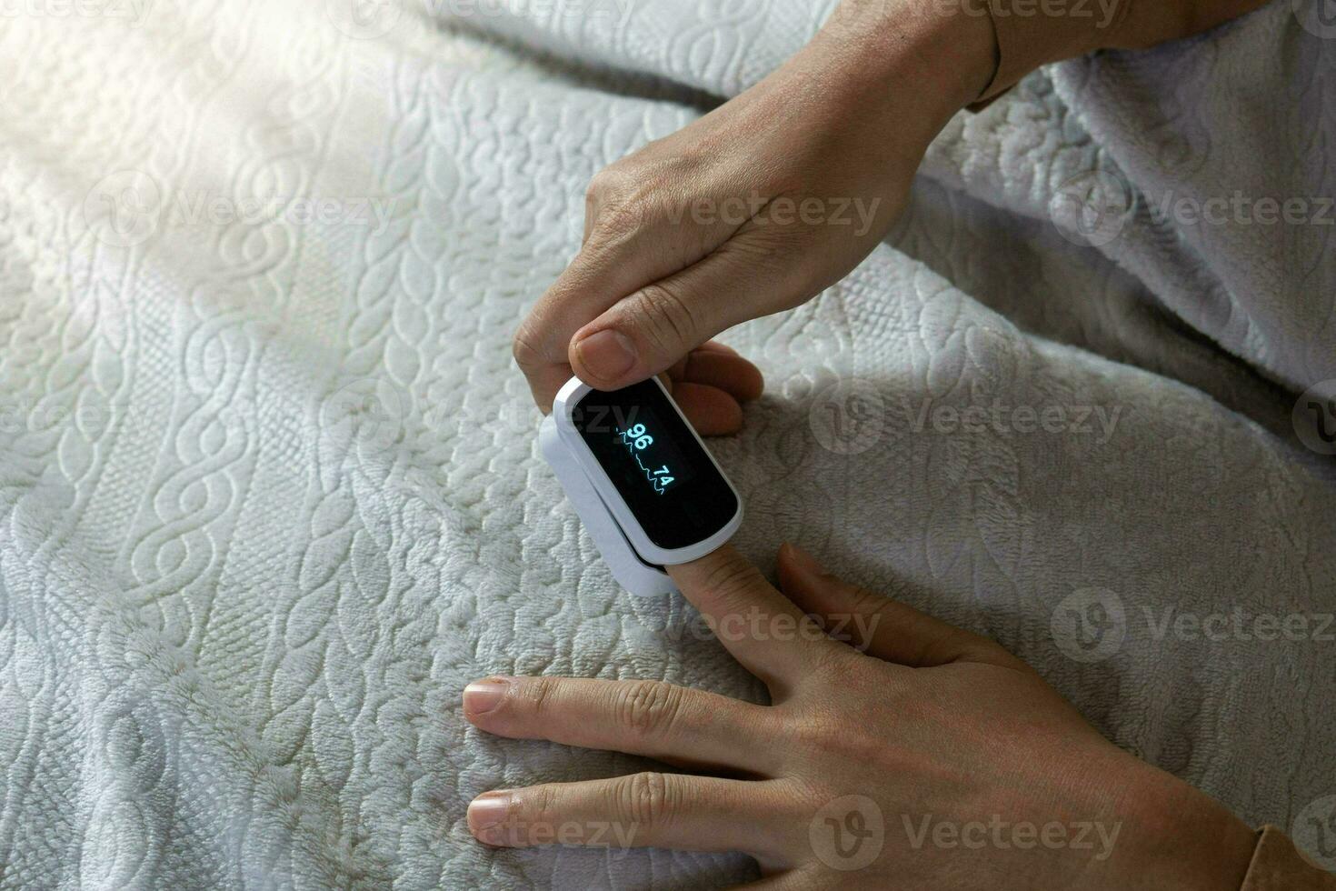 féminin mains avec une impulsion oxymètre à le indice doigt. femme mensonge à le lit. gadgets pour santé se soucier. concept de détermination de oxygène dans le sang. shotlistsanté photo