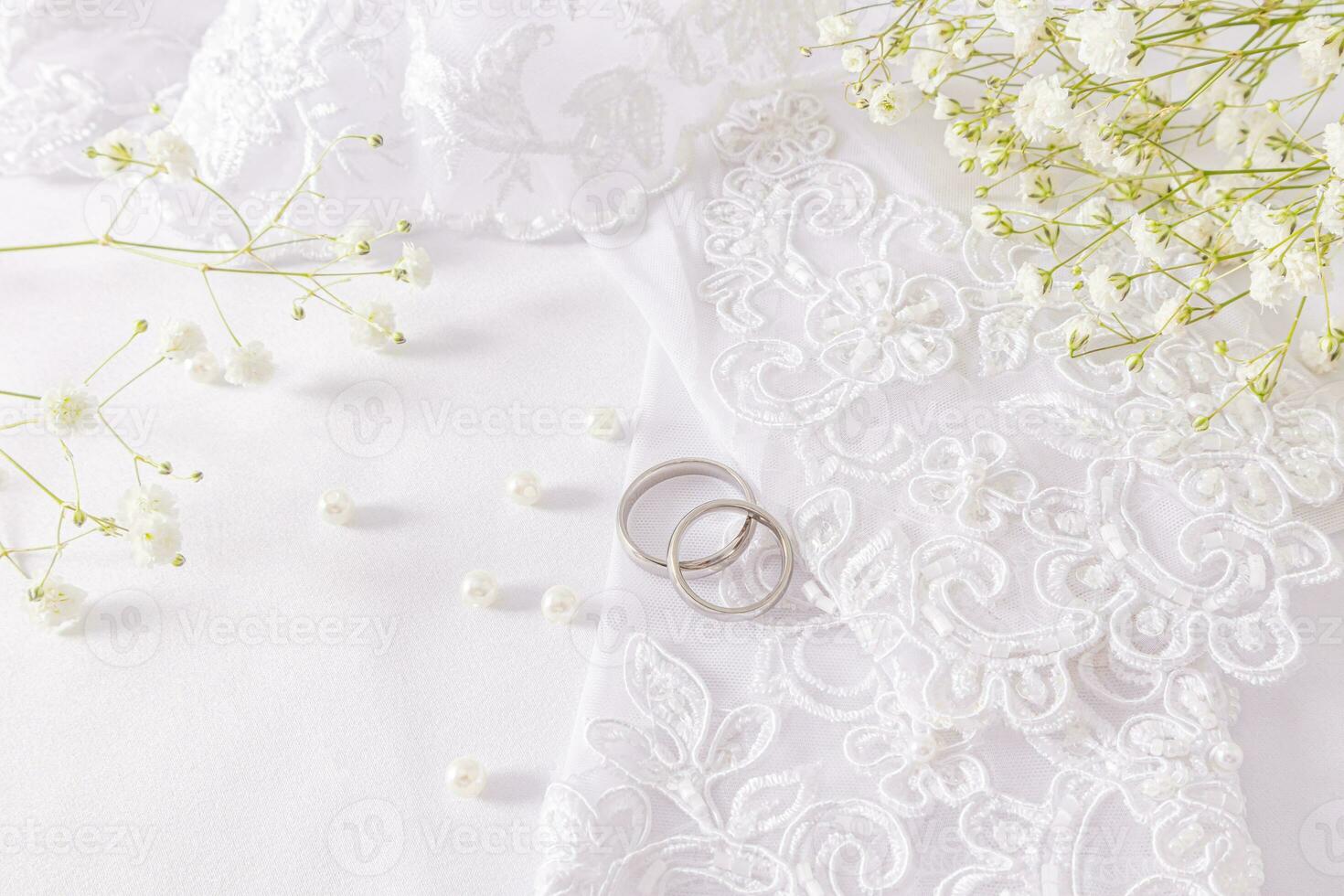 deux blanc or mariage anneaux mensonge sur le de la mariée blanc à motifs gants parmi perles de perles épars sur blanc satin. la mariée accessoires concept. photo