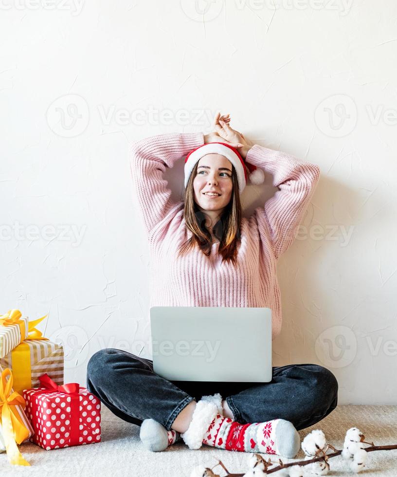 Jeune femme à santa hat shopping en ligne entourée de cadeaux photo