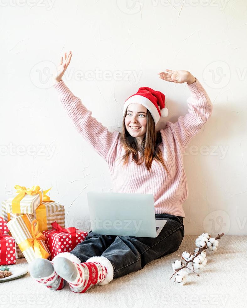 Jeune femme à santa hat shopping en ligne entourée de cadeaux photo