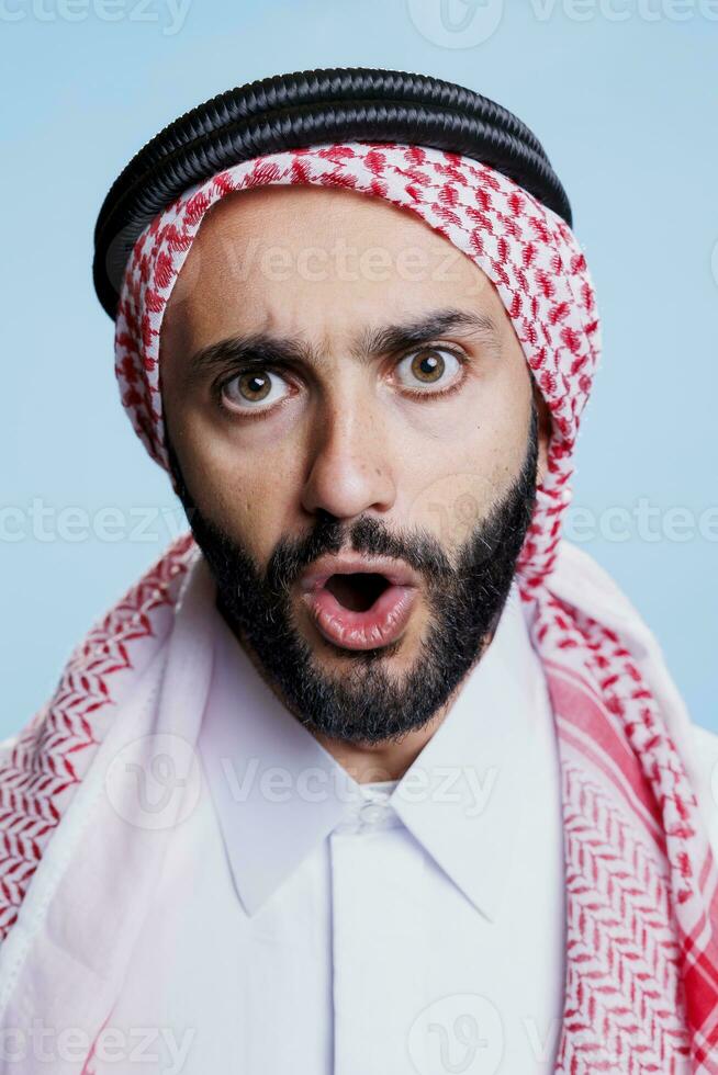 musulman homme avec ouvert bouche portant traditionnel à carreaux ghutra foulard studio fermer portrait. arabe la personne dans islamique coiffure montrant émotion sur visage et à la recherche à caméra photo