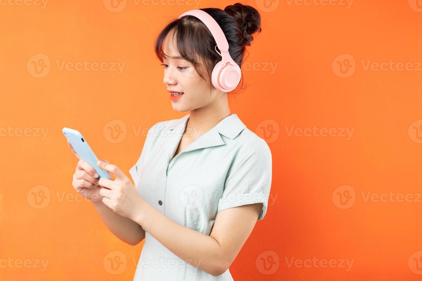 portrait de jeune fille utilisant le téléphone pour écouter de la musique, isolé sur fond orange photo