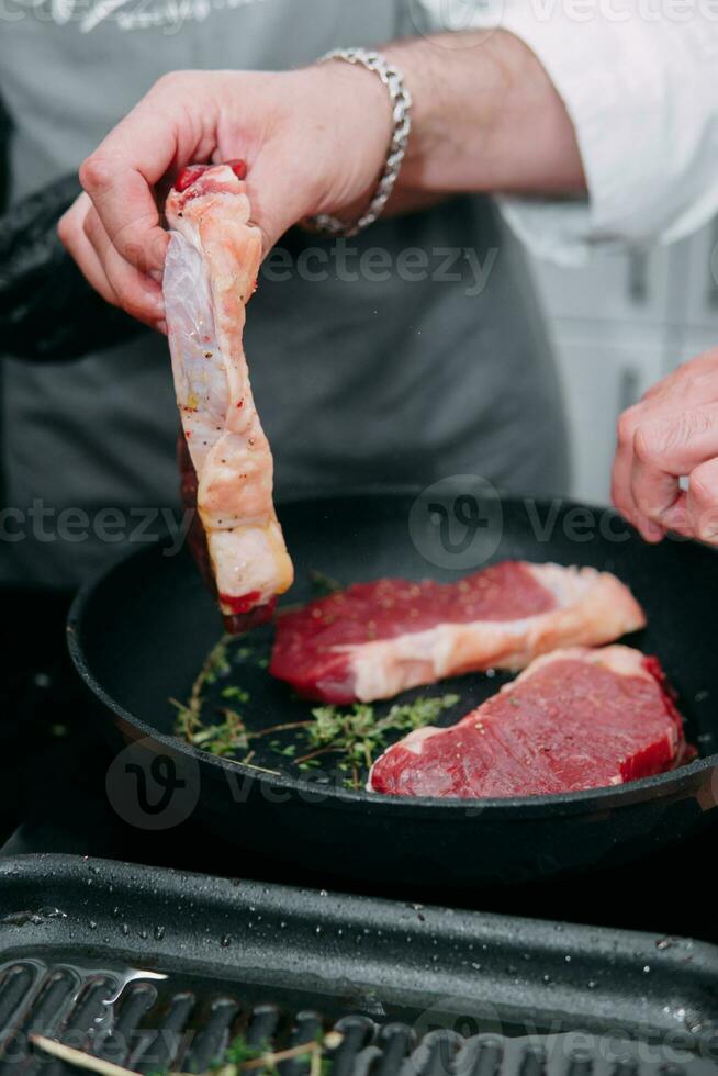 cuisine steaks dans une poêle. cuisine du boeuf à le culinaire Maître classe. le mains de le chef dans noir gants. photo