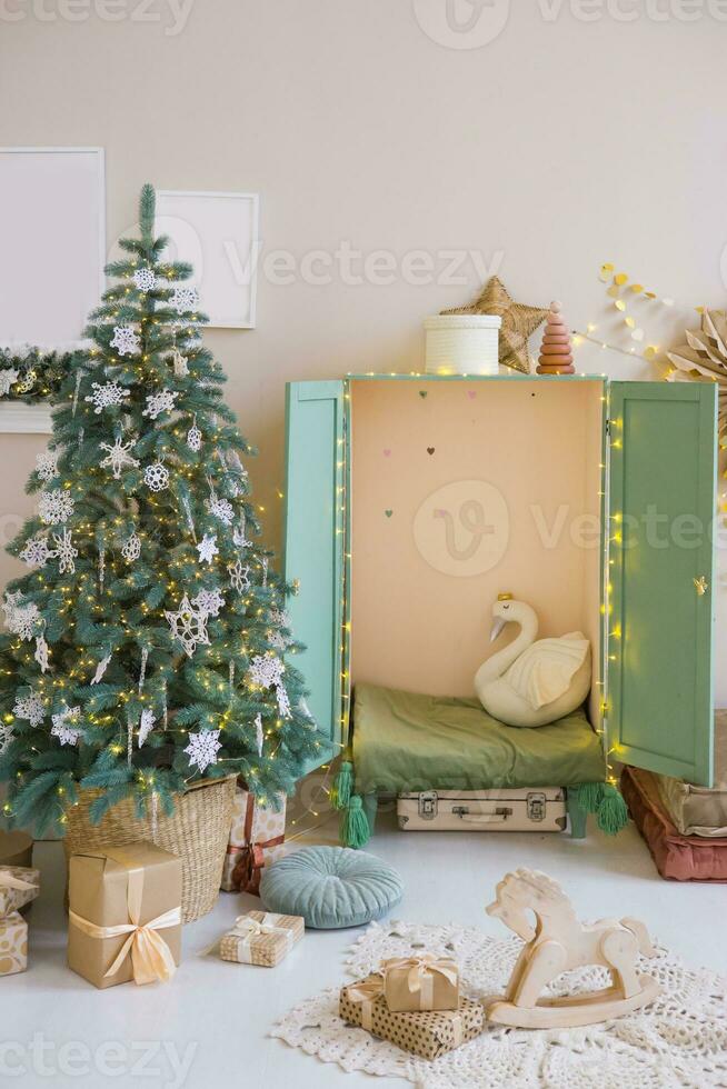 le intérieur de une enfants pièce décoré pour le Noël vacances. une Noël arbre avec guirlandes et une enfants garde-robe avec doux oreillers. photo