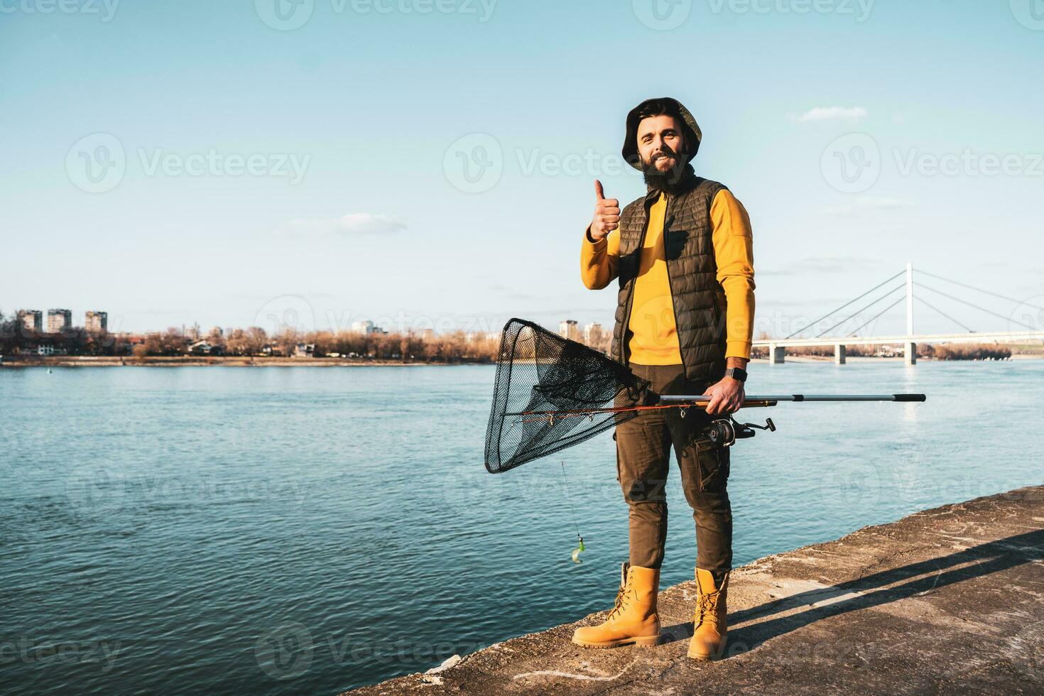 image de pêcheur avec pêche tacle montrant pouce en haut tandis que permanent par une rivière photo