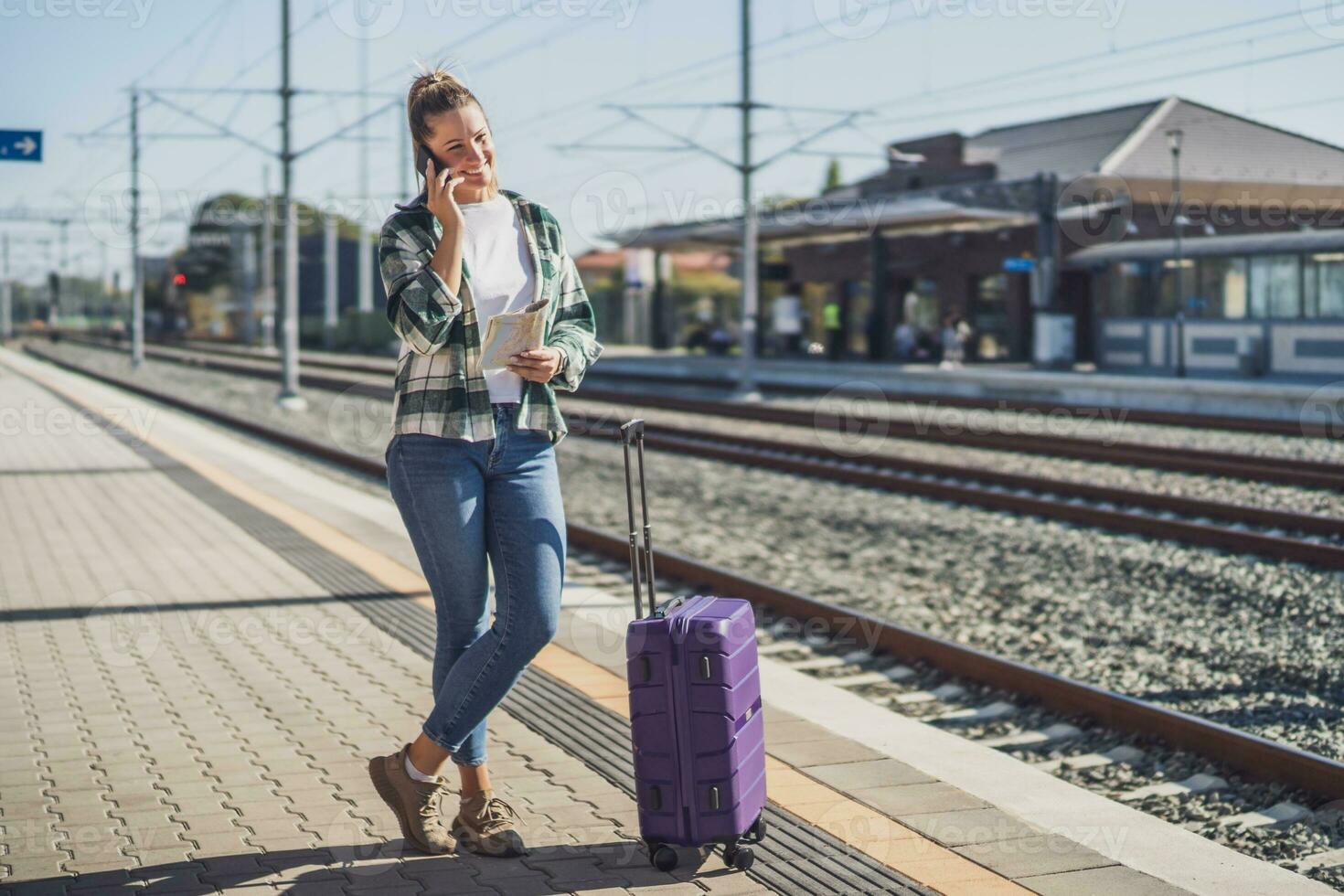 content femme en utilisant mobile téléphone et en portant carte sur une train station photo