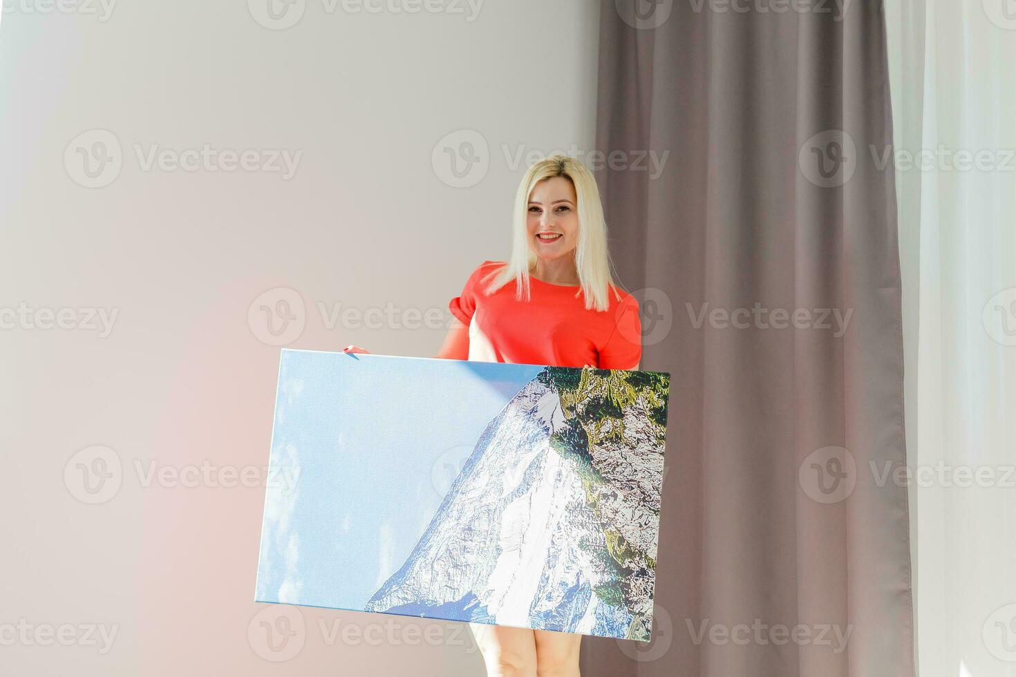 une content Jeune blond femme est en portant une grand mur photo Toile à Accueil
