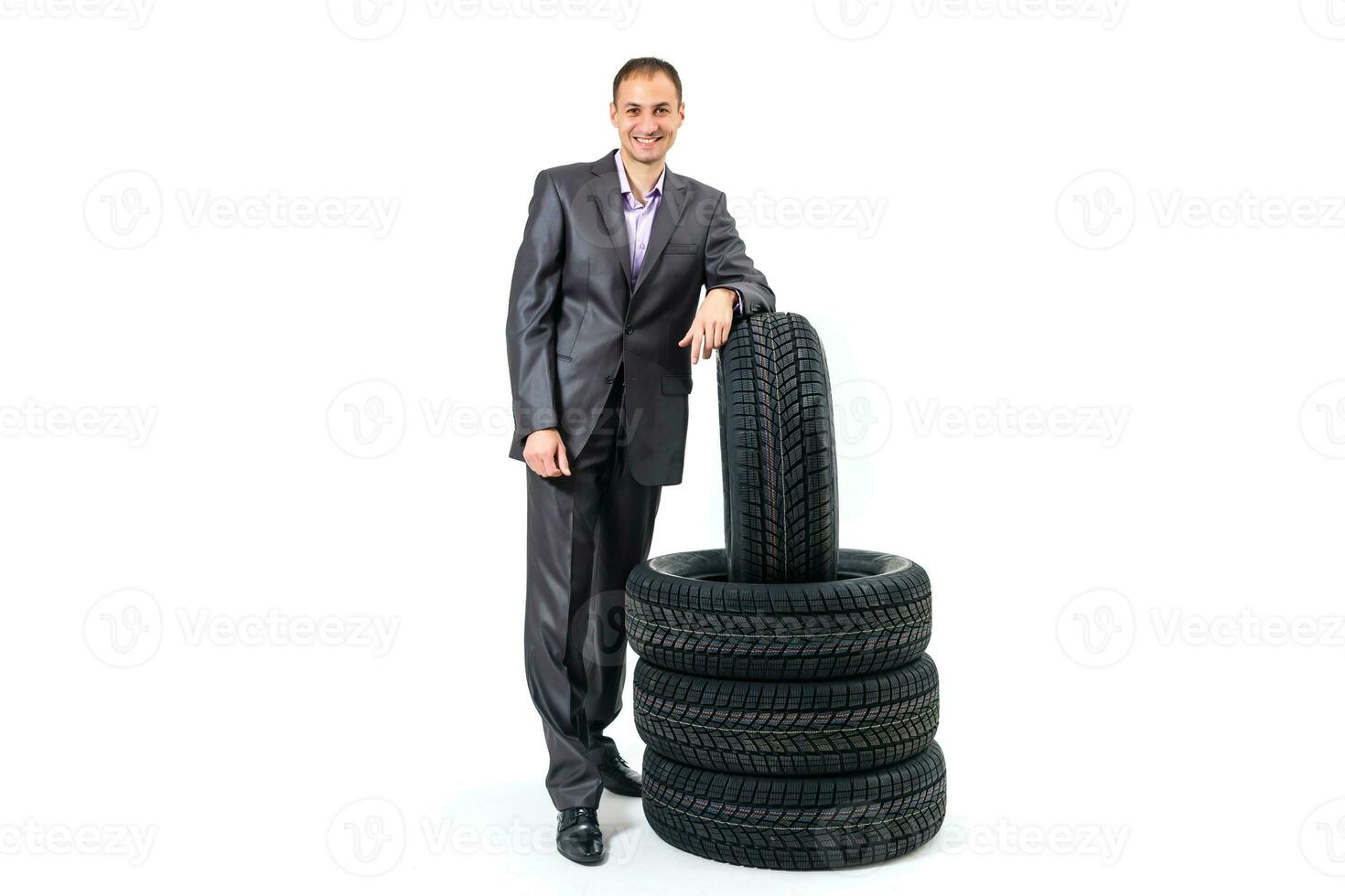 plein longueur portrait de une Jeune homme d'affaire penché sur une pile de voiture pneus isolé sur blanc Contexte photo