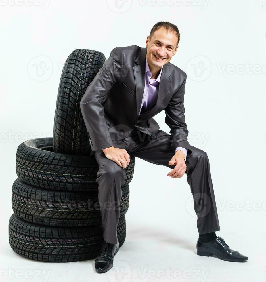 plein longueur portrait de une Jeune homme d'affaire penché sur une pile de voiture pneus isolé sur blanc Contexte photo