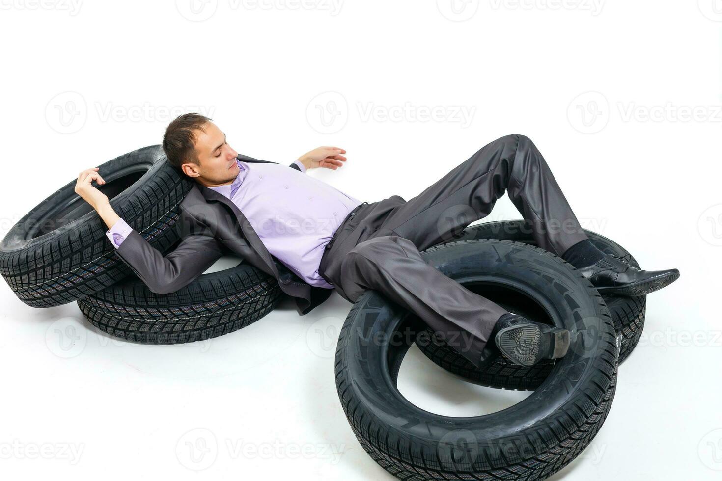 plein longueur portrait de une Jeune homme d'affaire penché sur une pile de voiture pneus isolé sur blanc Contexte photo