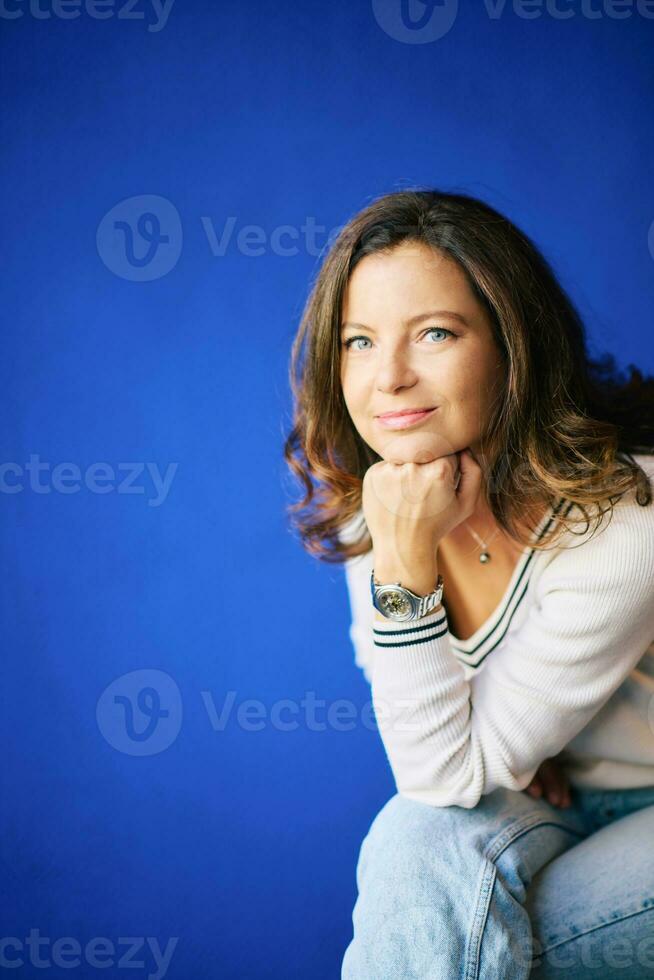 portrait de jolie 40 année vieux femme posant suivant à brillant bleu mur photo