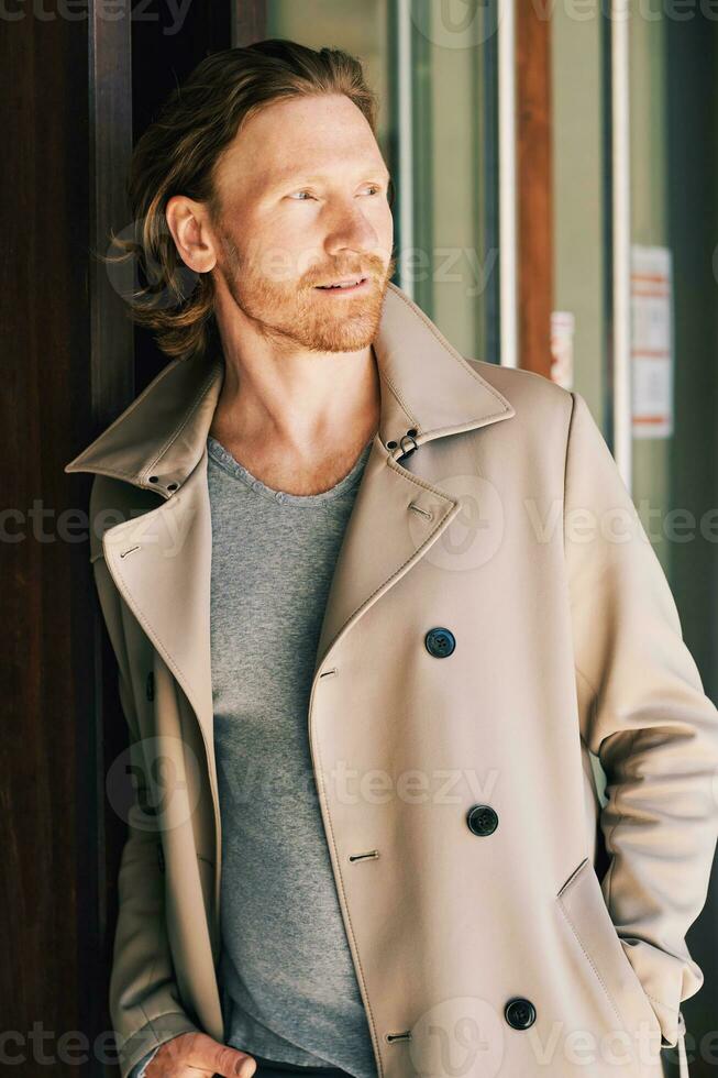 Extérieur portrait de Beau Jeune homme avec rouge cheveux, portant beige manteau, penché sur façade photo