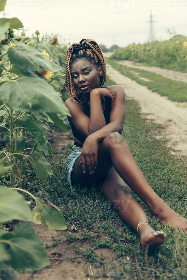 africain américain fille dans une champ de Jaune fleurs à le coucher du soleil photo