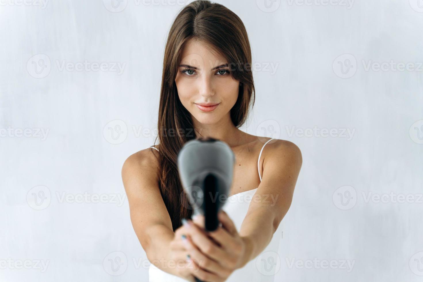 soin des cheveux. portrait de la jolie jeune femme posant pour la caméra avec un sèche-cheveux tout en le tenant comme une arme à feu. se concentrer sur les mains avec un sèche-linge photo