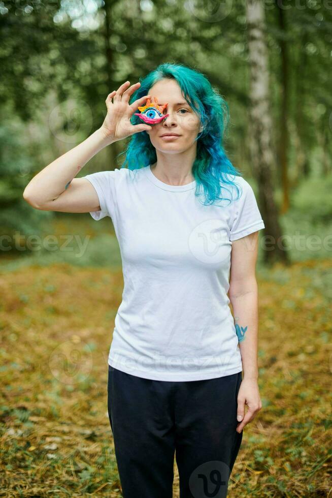 Jeune femme avec turquoise teint cheveux dans blanc t chemise détient Fait main coloré œil talisman photo