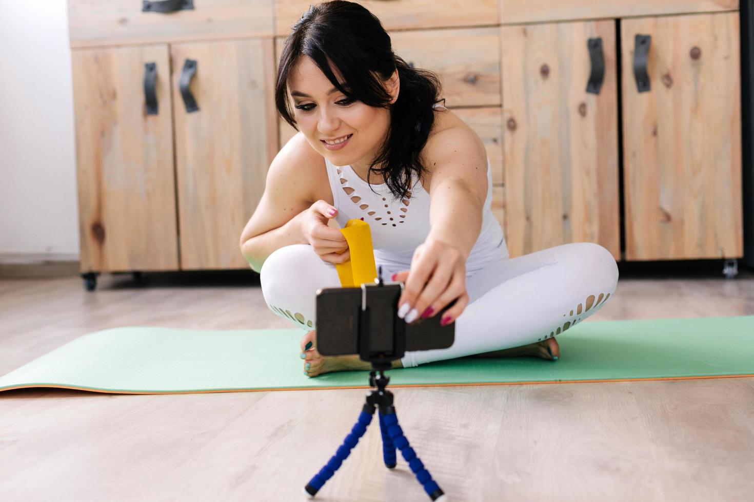 jeune femme portant des vêtements de sport blancs faisant du yoga assis en position du lotus, tourne une vidéo photo