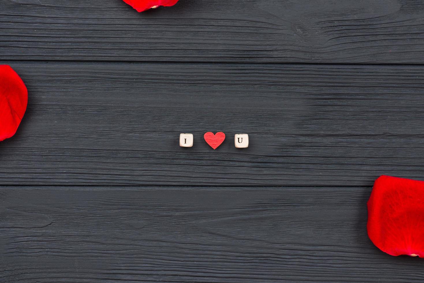 sur un fond en bois, la phrase je t'aime avec des cubes avec des lettres et des pétales de rose rouges. photo