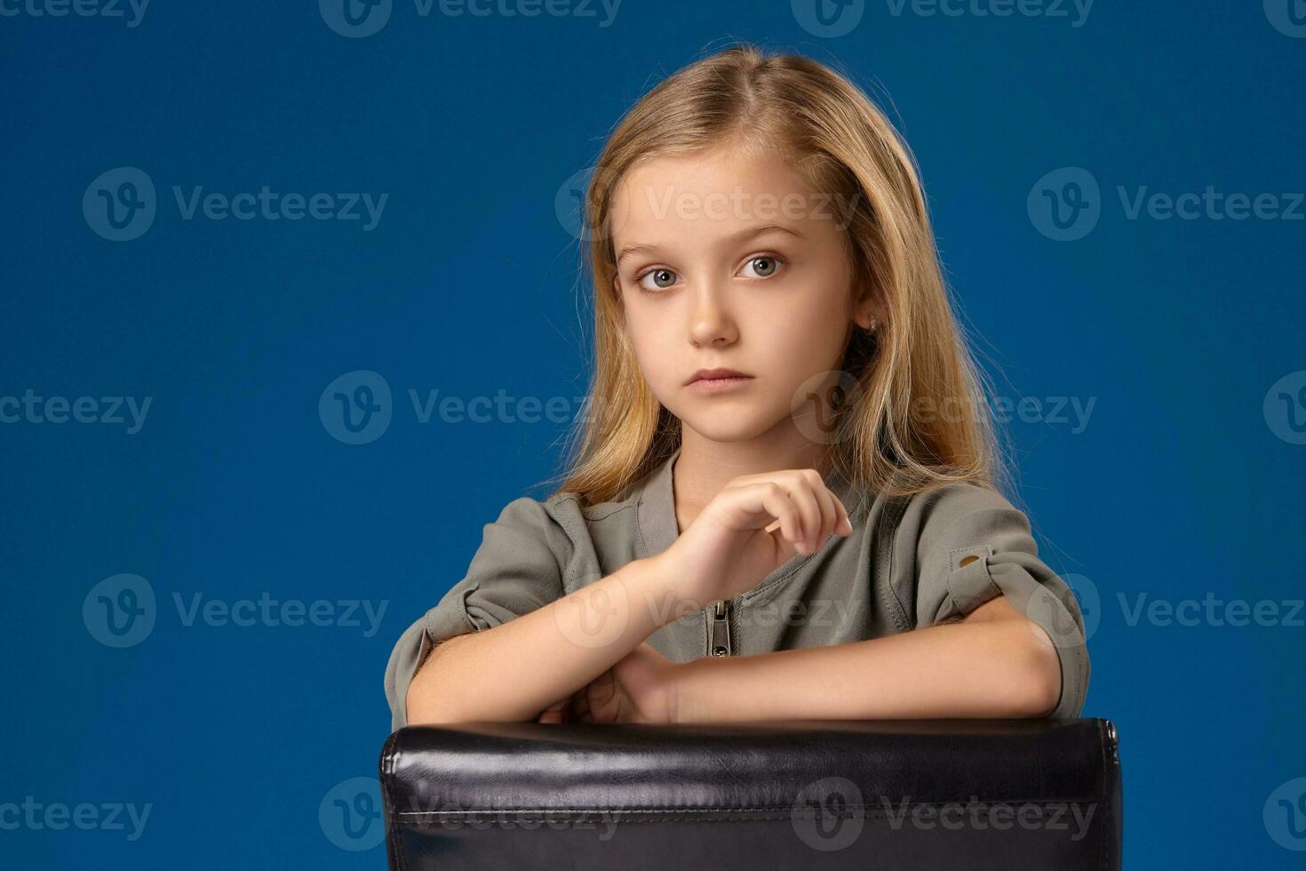 peu fille avec gris yeux et blond cheveux est assis sur une chaise photo