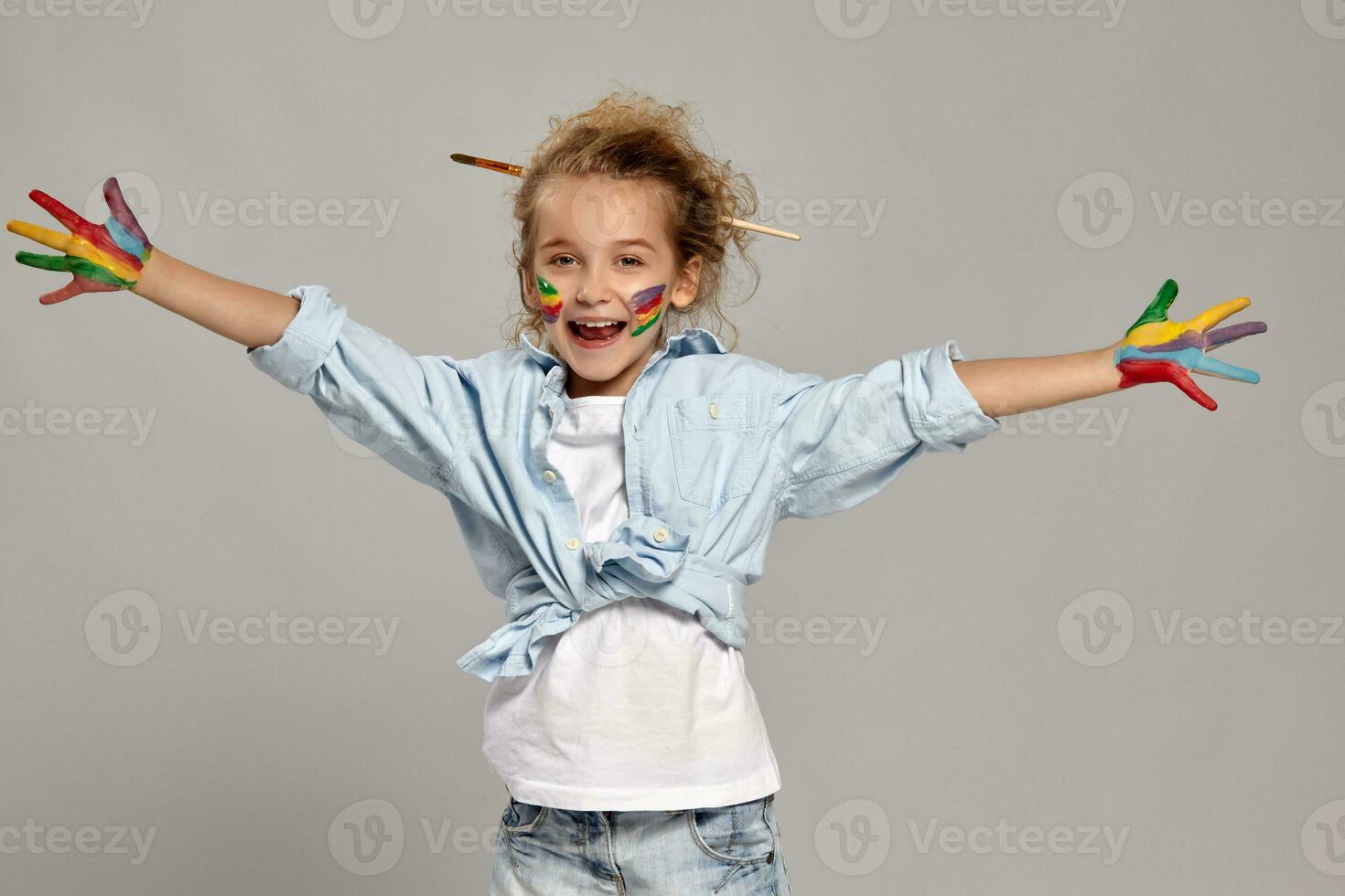 magnifique peu fille avec une peint mains et des joues est posant sur une gris Contexte. photo